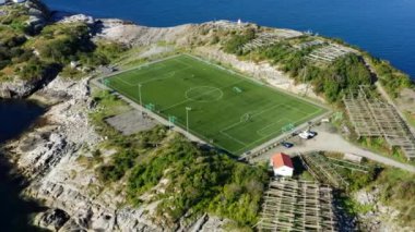 Okyanusun büyüleyici kucaklaşmasıyla iç içe geçmiş açık bir futbol stadyumunun havadan görüntüsü.