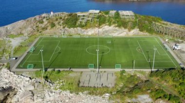 Uçsuz bucaksız mavi okyanusun nefes kesici arka planına karşı açık bir futbol sahasının havadan çekilmiş görüntüsü.