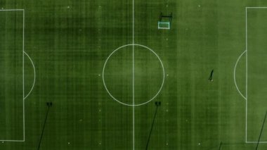 Bir futbol sahasının en üstteki görüntüsü yalnız bir insanın yürüyüşünü gösteriyor, sonra da yavaş yavaş sahanın orta çemberine doğru yaklaşıyor.