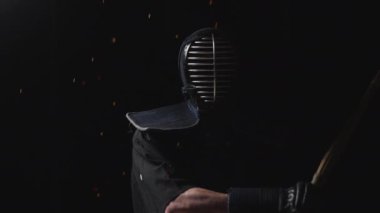 Geleneksel Kendogu kıyafetleriyle süslenmiş bir kendo ustası shinai 'sini siyah bir arka planda kıvılcımlar saçarak sallıyor.