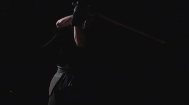 Geleneksel Kendogu ile süslenmiş kendini adamış bir pratisyen, shinai 'sini alevli kıvılcımlarla siyah bir zemin üzerinde zarif bir şekilde kullanır.