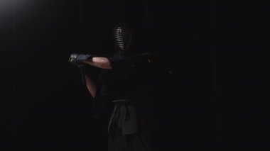 Kendo pratisyeni, geleneksel kendogu ile süslenmiş, shinai 'sini siyah bir arka planda ateşli kıvılcımlarla ustalıkla sallıyor.