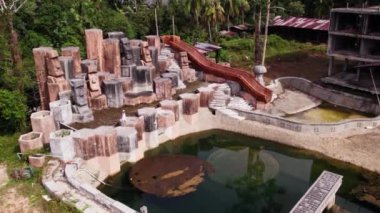 Beyaz elbiseli bir bayan Tayland 'ın başkenti Ko Chang' de bulunan yemyeşil palmiye ağaçları tarafından çerçevelenmiş terk edilmiş bir otel havuzunda taş kafalar arasında zarif bir şekilde yürüyor.