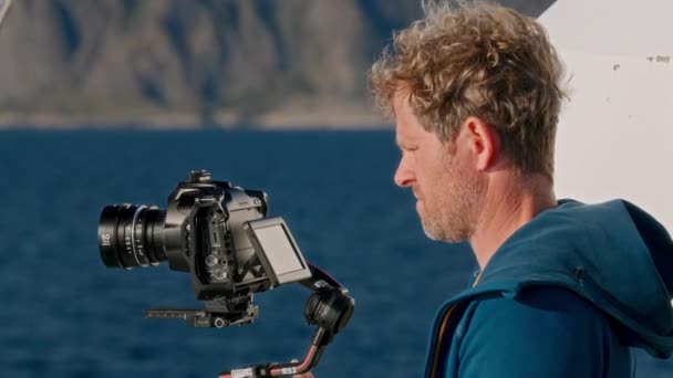 青いフードージャケットのフィルムメーカーは 海の畏敬の念を抱く美しさを巧みに捉え フェリーライド中にタワーアップする山を撮影します — ストック動画