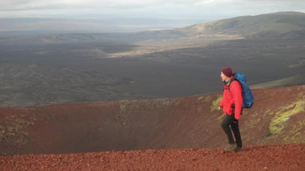 高齢のハイカーがラウダスカルクレーターの赤い火山の土を歩き 上空の広大な風景と曇りの空の背景に設定されています — ストック動画