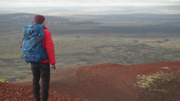 カメラがゆっくりとズームアウトするように ヒスラ火山の近くの広大な風景を賞賛するバックパックを持つ男の背中の景色 — ストック動画