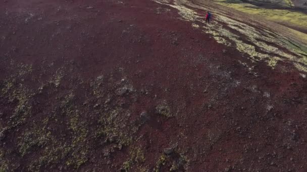 ラウダスカルクレーターのハイカーのチルトドローン映像は 下の広大な暗い火山の風景と上空の明るい空を示しています — ストック動画