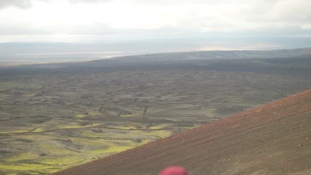 ボンネットとバックパックを着た男の背後からタイルショット 曇りの空の下のアイスランドのラウダスカルクレーターを取り囲む広大な景色を眺める — ストック動画