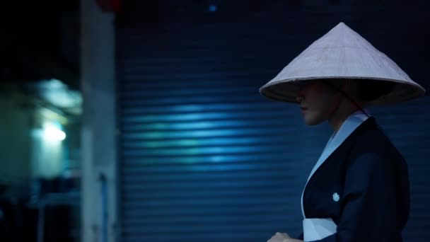 伝統的な着物に飾られた女性が 閉じたシャッターの近くで優雅に帽子をかぶり 謎と魅力を体現しました — ストック動画