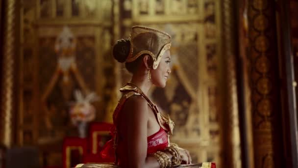 在一张侧面的照片中 一个身穿精美的金饰的女人优雅地坐在一座复杂的泰国寺庙里 — 图库视频影像