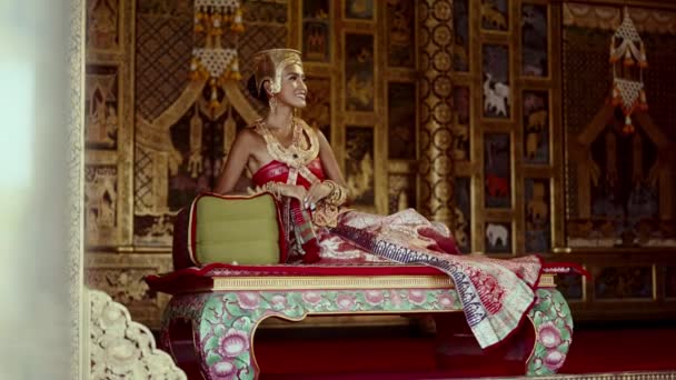 在泰国庙宇宁静的氛围中 一个女人装饰着精美的黄金饰物 坐在那里微笑着 — 图库视频影像