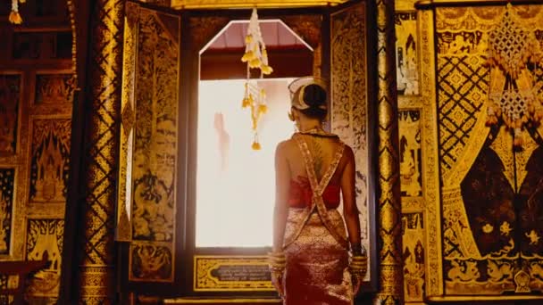 在一张背面的照片中 一个身穿传统泰式服装的女人优雅地从一座历史悠久的泰国寺庙的窗户向外张望 — 图库视频影像