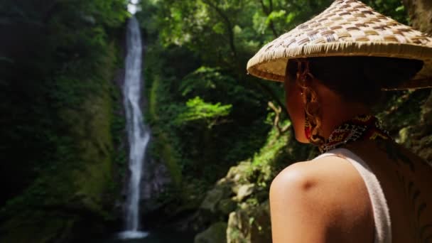 一个戴着草帽的女人的特写镜头 当她凝视着前面的瀑布时 她的纹身上闪烁着阳光 — 图库视频影像