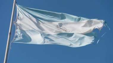 Açık mavi bir gökyüzünün altında rüzgarda sallanırken parçalanmış kenarları olan Arjantin bayrağının yakın çekimi