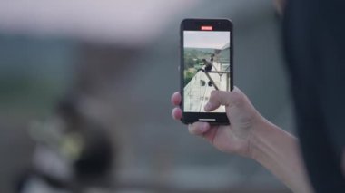 Bulanık bir arka planda bir maymunu çekerken elinde telefon tutan bir adamın yakın plan fotoğrafı.