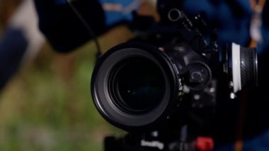 Gündüz vakti arkasında bulanık bir adam olan profesyonel bir kameranın yakın çekimi.