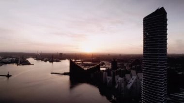 Aarhus Limanı 'ndaki modern mimarinin yanından geçen bir dronun yavaş çekim görüntüleri manzaralı bir günbatımı arka planına karşı