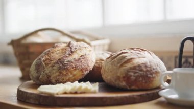 Taze pişmiş, gösterişli ekmek, tereyağı, Fransız pres bardağı ve beyaz bir fincan kahve ile yakın plan bir kahvaltı masası.
