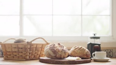 Mutfak tezgahında rahat bir kahvaltı sahnesi. Ekmek, tereyağı, kahve ve doğal ışığı olan bir pencere.