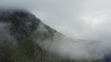 İnsansız hava aracı göksel bulutlarla çevrili bir dağın üzerinden süzülüyor.