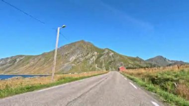 Lofoten 'ın kıyı yolu boyunca nefes kesen dağ manzarasını gösteren bir gündüz videosu.