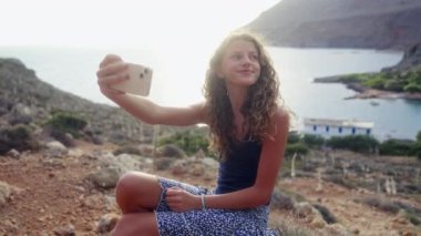 Mavi bluzlu bir kız selfie sanatını benimsiyor. Huzurlu sahil manzarasına karşı unutulmaz anlar yaratıyor.
