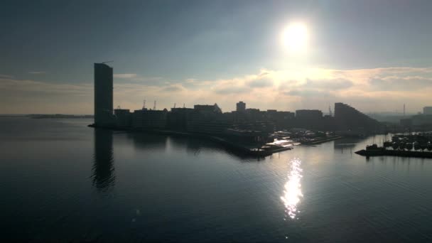 ドローンが水の上を飛び 下の高層ビルと港の上に輝く輝く輝かしい日没を捉える — ストック動画
