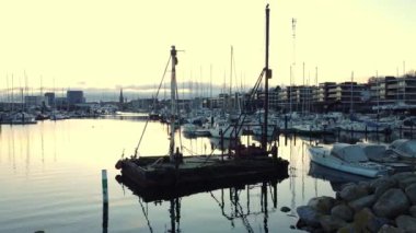 Gün batımında kayaların ve küçük teknelerin yanında bir mavna yüzer.