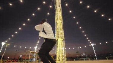 Işıklarla süslenmiş bir parkta break dans yaparken dönen şık bir dansçının düşük açılı çekimi.