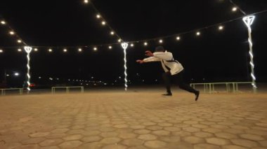 Bir break dansçı, parlak park ışıkları altında karmaşık bir ters takla gösterisi yaptıktan sonra poz verir.