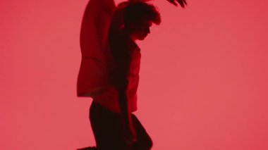 Genç bir adam kırmızı arka planla aydınlatılmış sahnede dans ederken kollarını ve vücudunu çeviriyor.