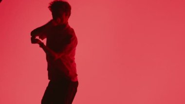 Silüet giymiş genç bir adam elleri parlak kırmızı bir arka planda karmaşık hip-hop dansları yapıyor.