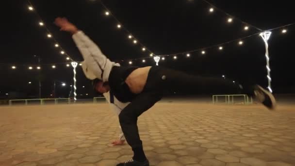 夜のパークライトの下でフリースタイルが動く複雑なブレイクダンサーのパンニングショット — ストック動画