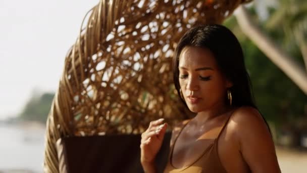 日落时 一位女士优雅地坐在沙滩上悬挂的藤椅上摆姿势 — 图库视频影像