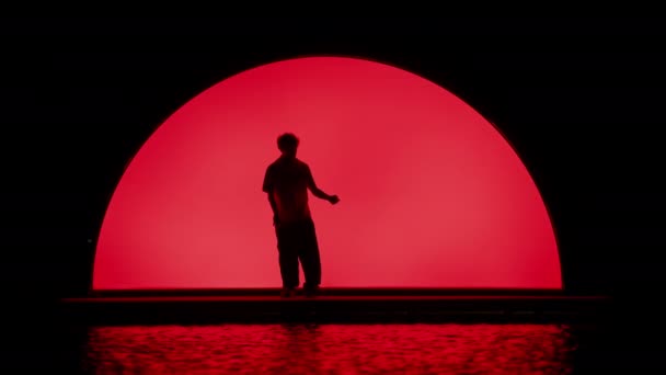 一个男人的轮廓被描绘成在舞台上跳舞 红色的拱门从后面发出光芒 产生光晕效果 — 图库视频影像