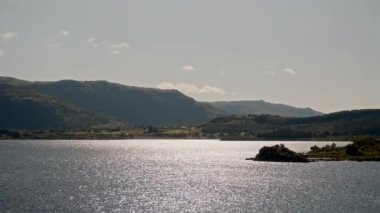 Gündüz vakti göz kamaştırıcı İskandinav manzaralarıyla çevrili ışıl ışıl bir göl gösteren huzurlu ve güzel bir manzara.