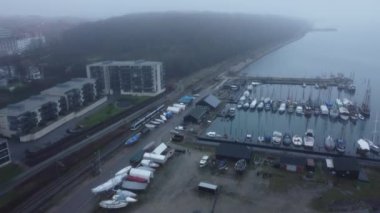 Bir dron rıhtımdaki teknelerin üzerinde uçuyor, liman şehrinde sisle kaplı bir treni takip ediyor.