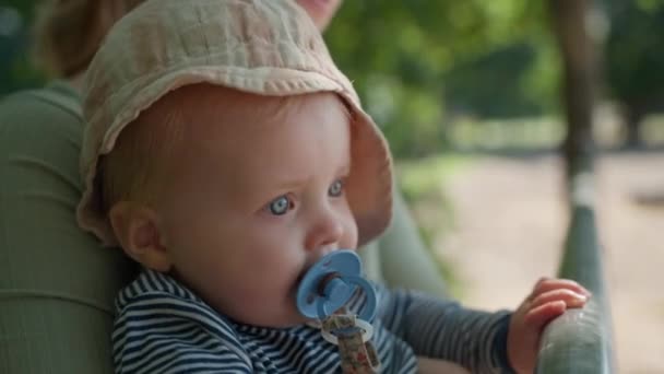 一个戴着帽子的可爱婴儿的特写镜头 吸吮着甲醚 牵着农场围栏 同时被他的母亲抱着 — 图库视频影像