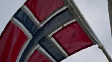 Norveç bayrağının bir direğin üstünde yakın plan çekimi, rüzgarda dalgalanan mavi bir gökyüzünün arka planına karşı