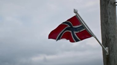 Norveç bayrağı direğin tepesinde dalgalanır, rüzgarda dalgalanır bulutlu gökyüzünün arka planında