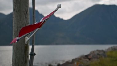 Bir Norveç bayrağı, bulutlu bir gökyüzünün altında bir dağın arka planına karşı rüzgarda sallanıyor.