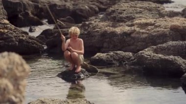 Genç bir çocuk gün boyunca geleneksel bir tahta çubuk kullanarak ustalıkla kayadan balık tutuyor.