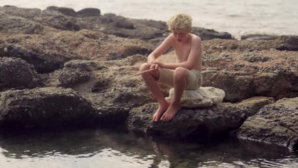 Mladý Chlapec Sedící Skalnatém Pobřeží Zabývající Uměním Rybaření Pokornou Holí — Stock video