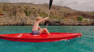 Girit 'in sakin sularında engebeli kayalara karşı kano yolculuğuna çıkmış genç bir çocuk.