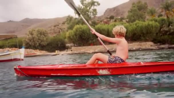 Young Boy Navigates Waters Crete Vibrant Red Kayak Amidst Breathtaking — Stock Video
