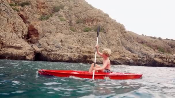Young Boy Navigates Waters Crete Bright Red Kayak Rocky Mediterranean — Stock Video