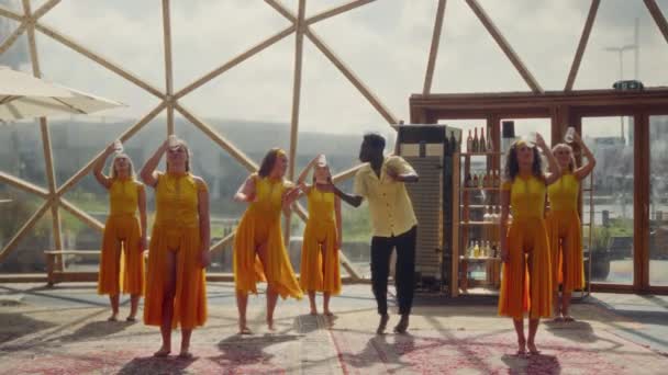 这是一个静态镜头 拍摄到穿着橙色衣服 手持塑料杯的熟练舞者 展示了他们在独特的大地测量穹顶框架内的非凡才华 — 图库视频影像