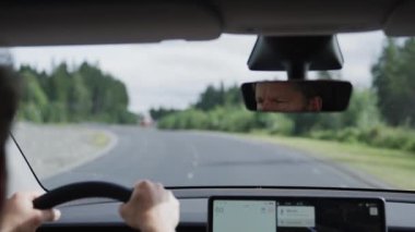 Elektrikli araba kullanan bir adam dikiz aynasından süzülürken, gür, canlı ağaçlar tarafından kucaklanan, sürdürülebilir yolculuğu doğal sükunetle uyumlu hale getiren sakin yollarda görülür.