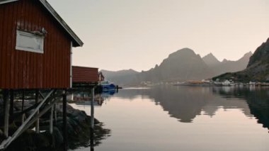 Lofoten 'da bir balıkçı köyünü uzak bir dağ manzarasının önünde soldan sağa hareket eden bir tava görüntüsü.