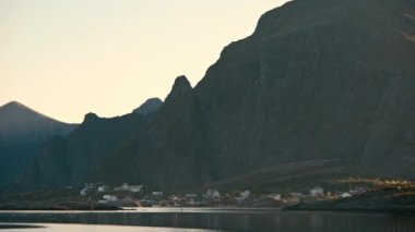 Soldan sağa yayılan bir panoramik çekim, Lofoten 'de dağlık bir zemin ile bir balıkçı köyünü yakalıyor.